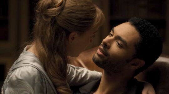 Een vrouw zit op schoot bij een man en ze kijken elkaar aan.