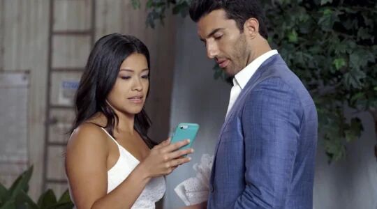 Jane kijkt op haar telefoon terwijl Raphael naast haar staat.