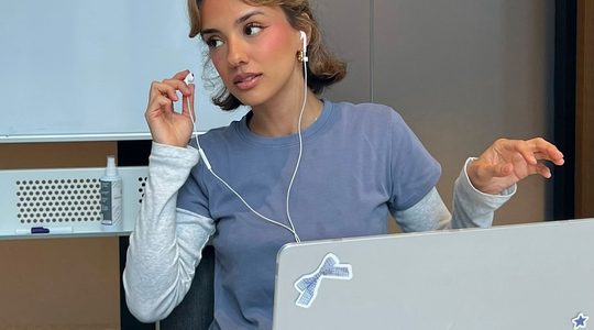 Influencer Kika Lateef zit achter laptop, ze doet haar oortje uit.