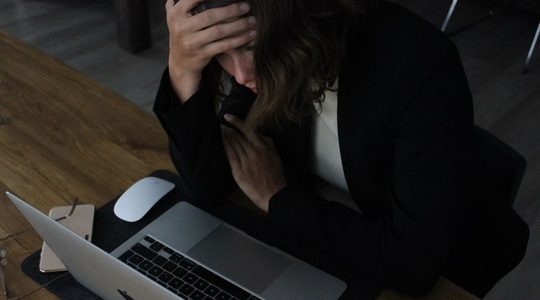 Vrouw die gestresst achter haar laptop zit.
