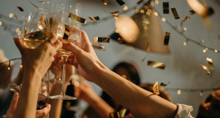 Mensen heffen hun champagneglazen en proosten, terwijl confetti naar beneden valt.