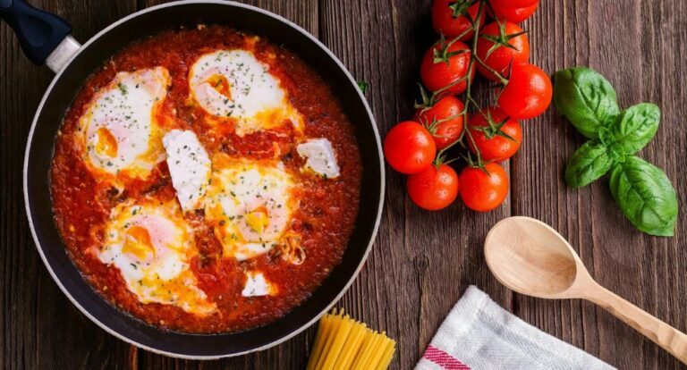 Gerecht met burrata in tomatensaus, met tomaatjes en een pollepel ernaast.