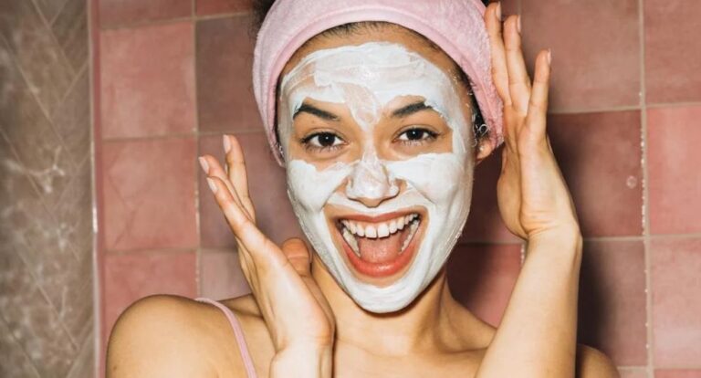 Lachende vrouw met een gezichtsmasker en een handdoek om haar haren.