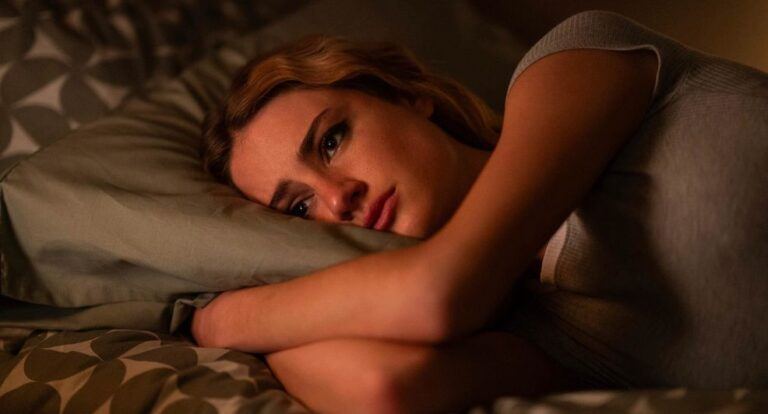 Een jonge vrouw ligt emotioneel op bed.