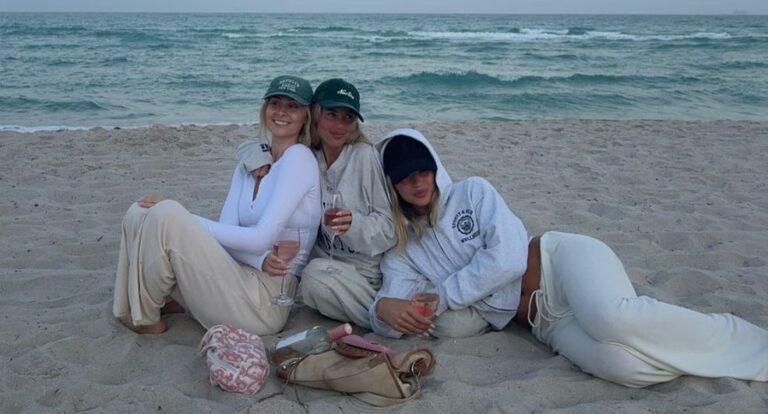 Drie meiden lachend op het strand met een glas wijn.