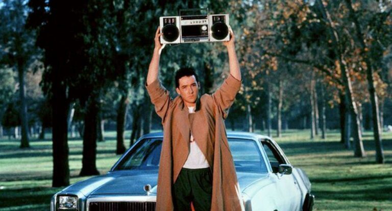 Man staat met een boombox voor een oude auto.