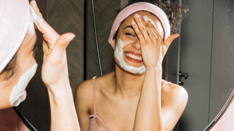 Een vrouw doet een gezichtsmasker op in de spiegel.