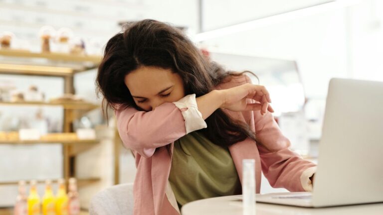 Vrouw niest in ellenboog achter laptop