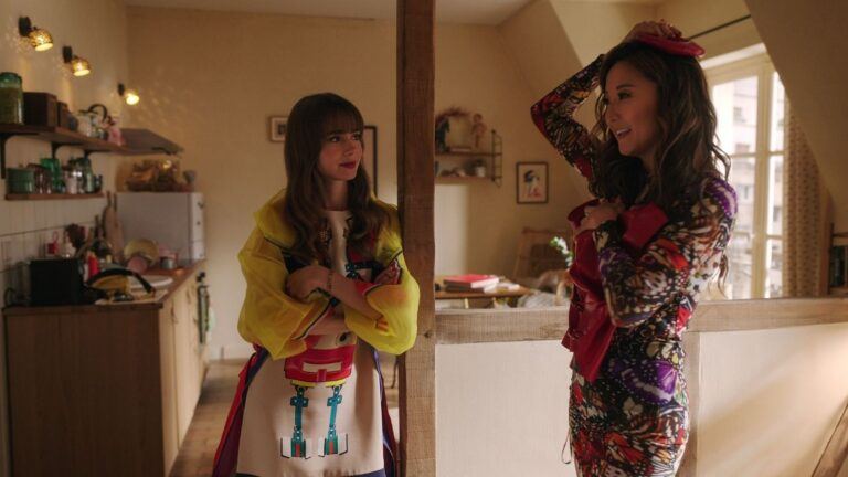 Emily en Mindy uit Emily in Paris staan in hun kleine appartement.