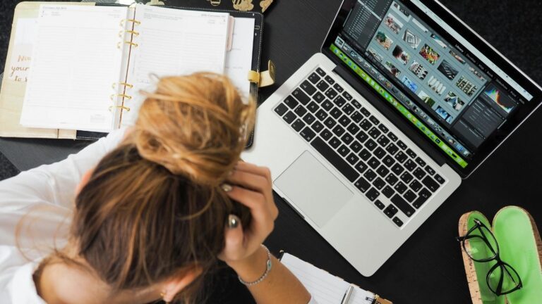 Een vrouw zit achter haar laptop met haar handen in haar haren.