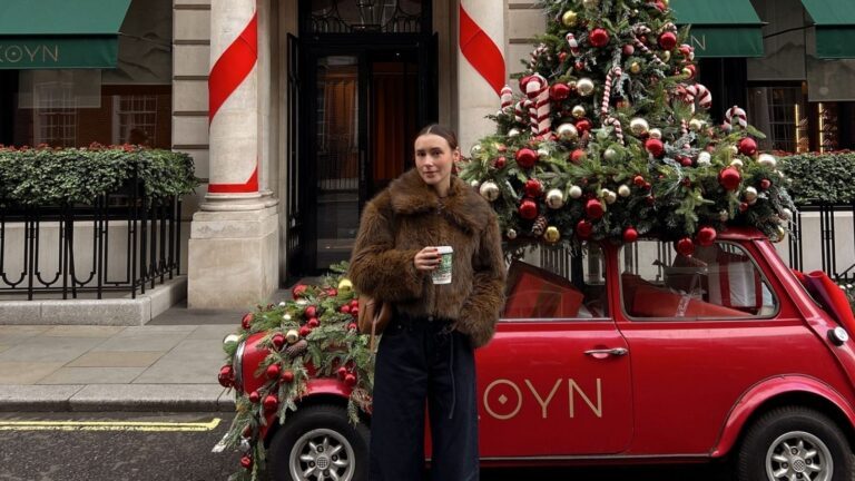 Meisje staat in Londen voor een auto met een kerstboom erop.