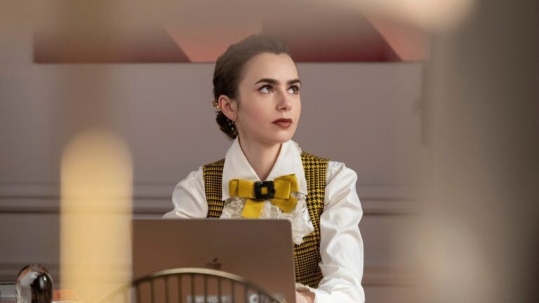 Emily uit Emily in Paris achter haar bureau.