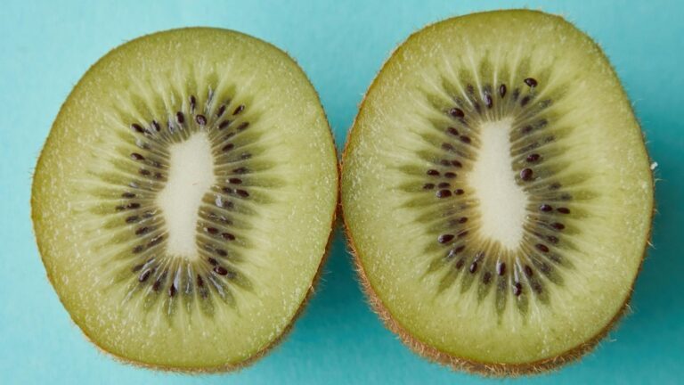 Een opengesneden kiwi met een blauwe achtergrond.