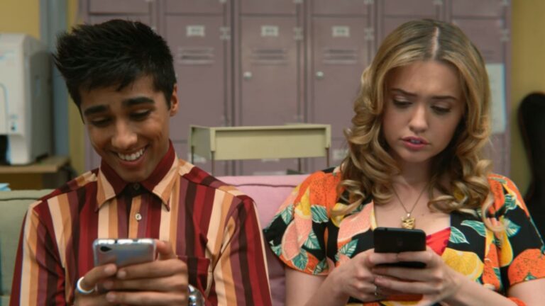 Sc&egrave;ne uit de serie: Sex Education. Een meisje en een jongen kijken op hun telefoon. De jongen lacht naar zijn scherm, het meisje kijkt verbaasd naar haar scherm.