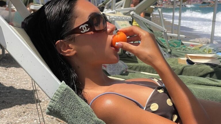 Vrouw ligt op een strandbed. Ze eet een appel.