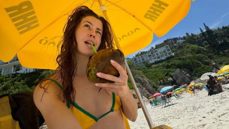 Een meisje drinkt uit een kokosnoot op het strand.