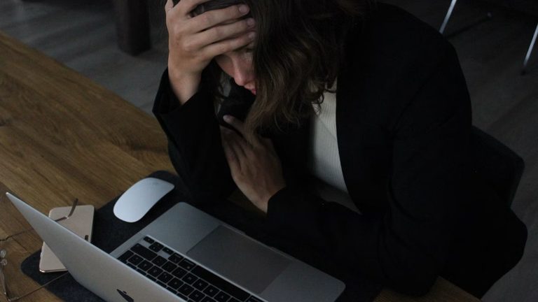 Vrouw die gestresst achter haar laptop zit.