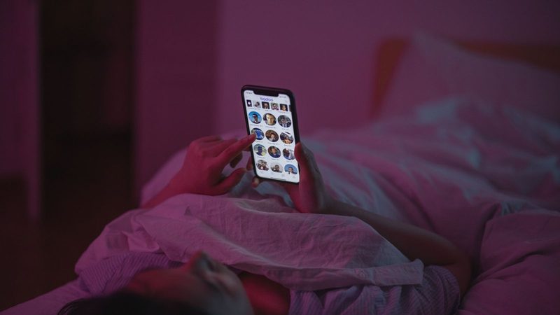 Iemand ligt in bed met zijn telefoon.