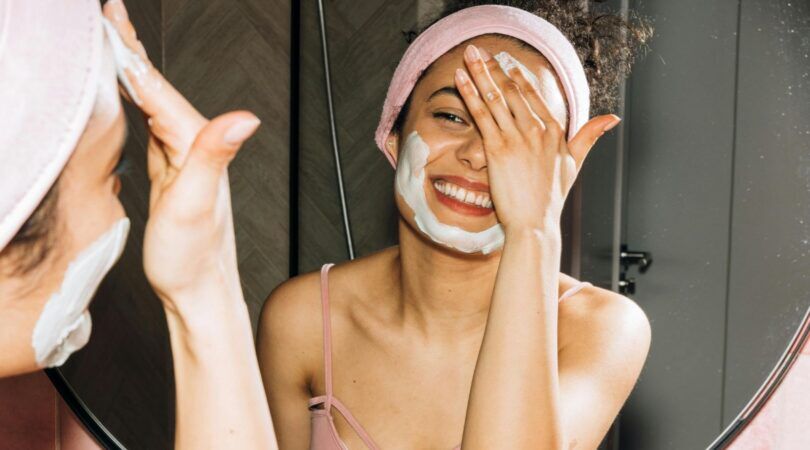 Een vrouw doet een gezichtsmasker op in de spiegel.