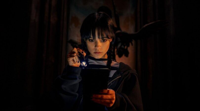 Wednesday Addams zit in haar kamer met een zaklamp.