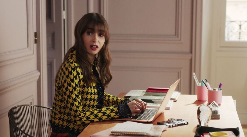 Sc&egrave;ne uit Emily in Paris waar Emily achter haar bureau zit.