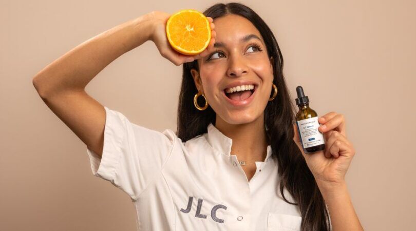 Jonge vrouw met een sinaasappel en een Vitamine C serum in haar handen.