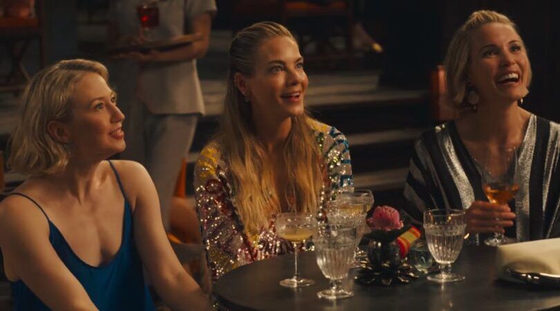 Sc&egrave;ne uit The White Lotus waar drie vrouwen op een rijtje zitten en lachen.