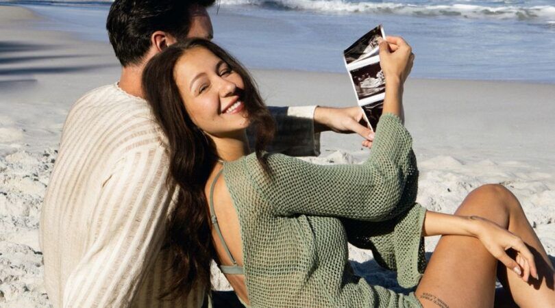 Sophie Milzink en haar vriend Brian zitten samen op het strand met een babyecho in de hand.