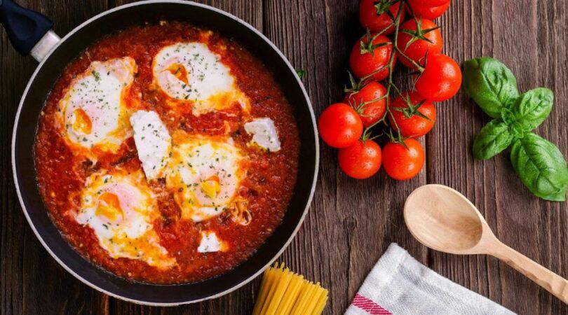 Gerecht met burrata in tomatensaus, met tomaatjes en een pollepel ernaast.