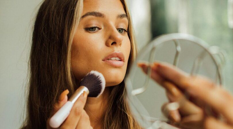 Een vrouw die haar make-up aan het doen is terwijl ze in een spiegel kijkt.