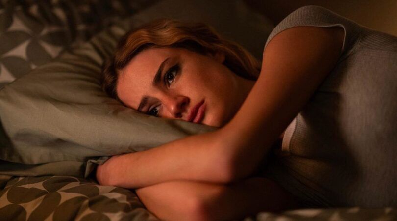 Een jonge vrouw ligt emotioneel op bed.