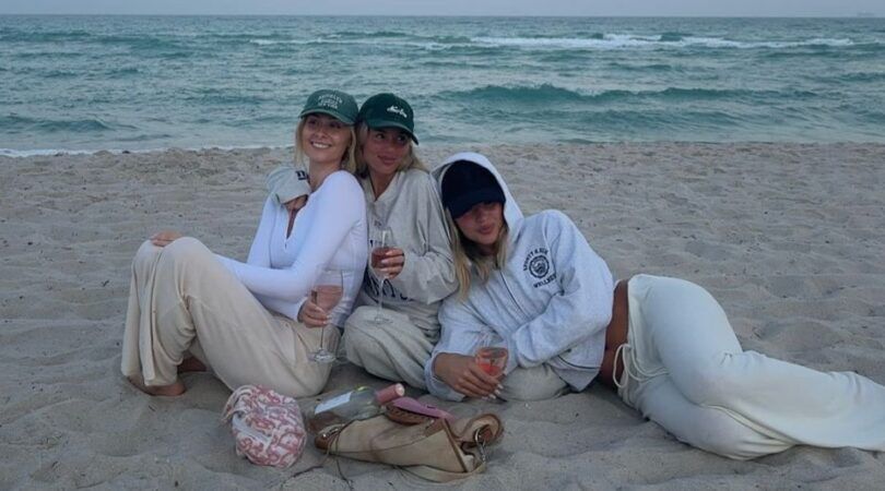 Drie meiden lachend op het strand met een glas wijn.