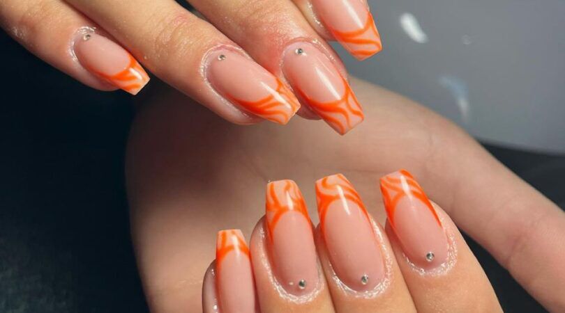 Twee handen met oranje nailart op de nagels.