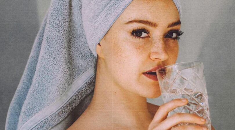Een vrouw die water drinkt, met een handdoek op haar hoofd.