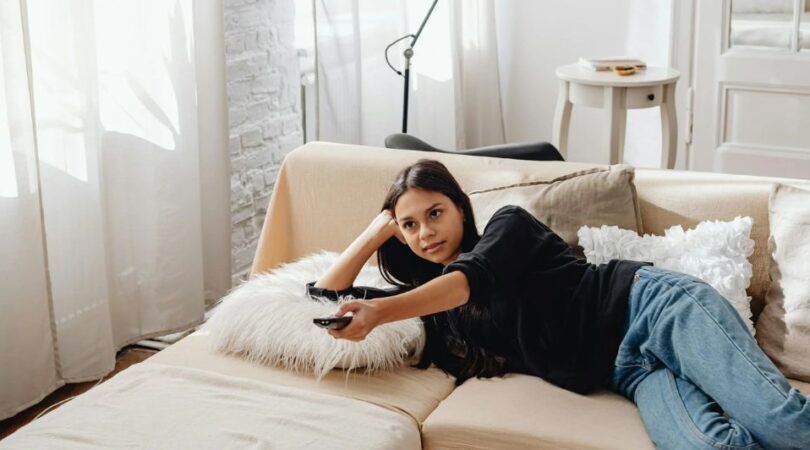 Een meisje die op de bank ligt terwijl ze tv kijkt.