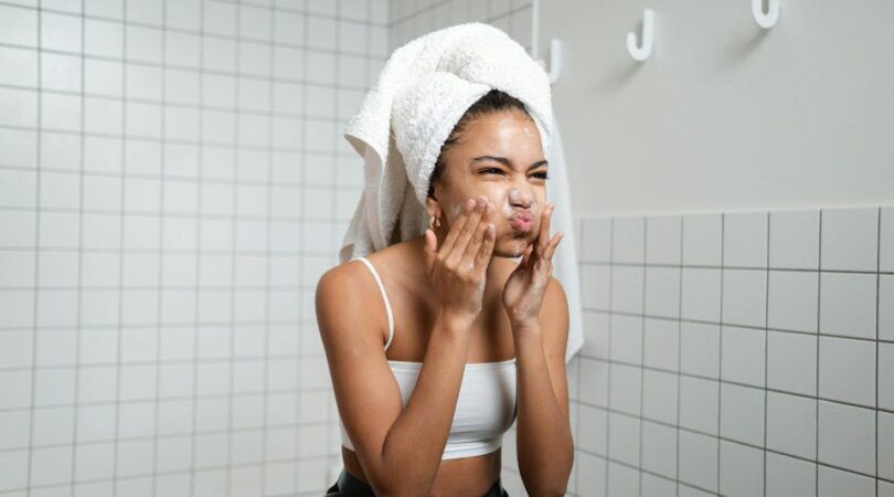 Een meisje die met een handdoek op haar hoofd haar gezicht aan het reinigen is.