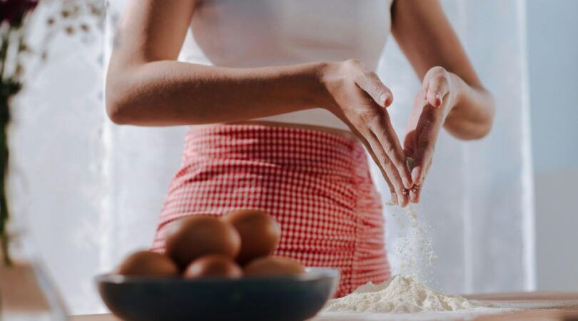 Een vrouw die aan het bakken is en bloem over het aanrecht strooit.