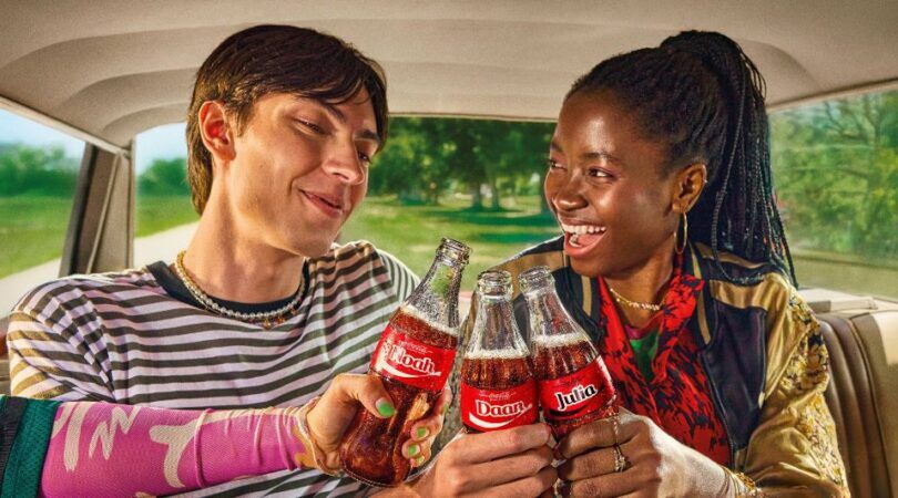 Een vrouw en een man die hun Coca-Cola flesje proosten.