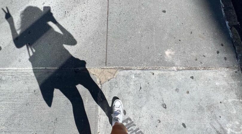 Ashley Alexander die aan het wandelen is en een selfie maakt van haar schaduw, terwijl ze een peace teken opsteekt.