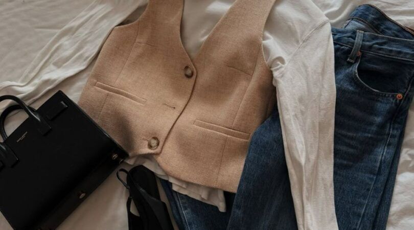 Kledingstukken en een tasje op een bed.