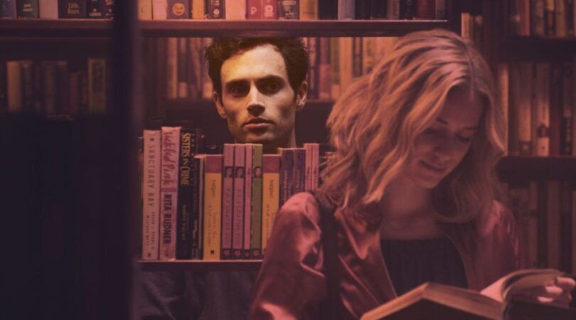 Man die door een boekenkast stiekem naar een vrouw kijkt.