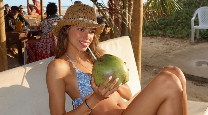 Een vrouw die op een strandbedje uit een kokosnoot drinkt.