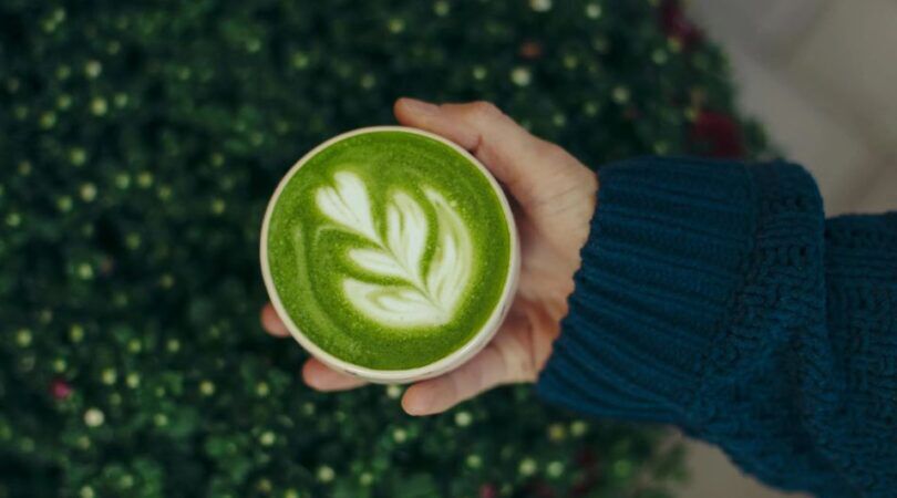 Een hand houdt een kopje matchakoffie vast.