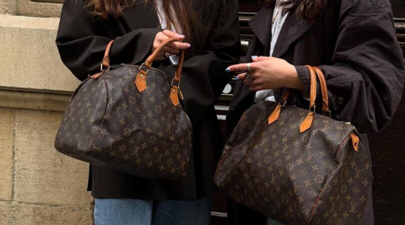 2 meiden die naast elkaar staan met allebei een grote Louis Vuitton tas in hun handen.