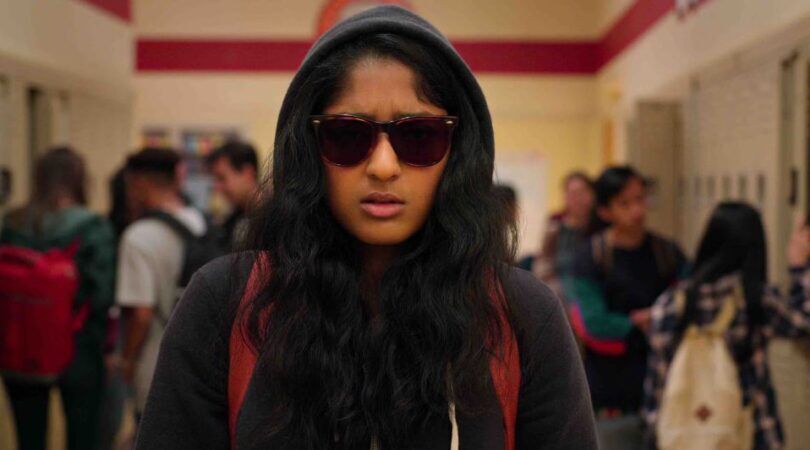 Sc&egrave;ne uit Never Have I Ever waar Devi met capuchon omhoog en zonnebril op door de schoolgangen loopt.