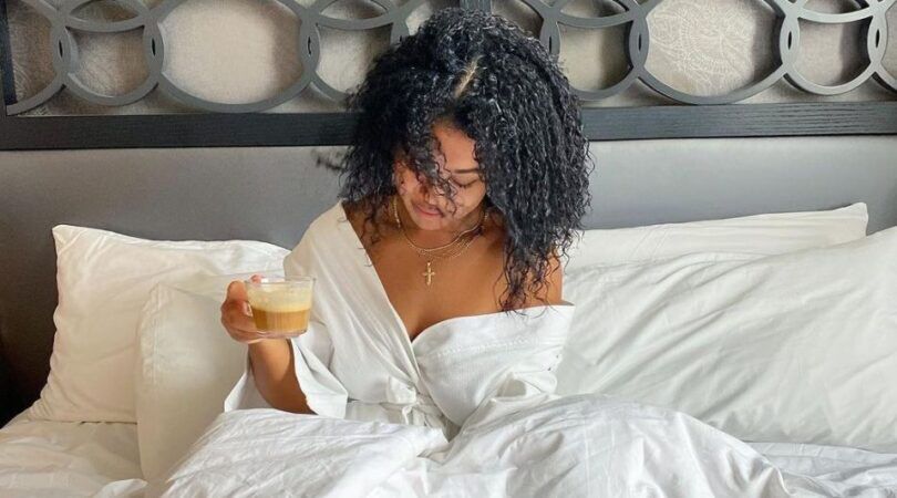 Een vrouw die in bed zit met een koffie in haar hand.