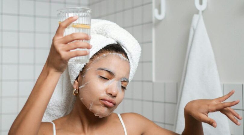 Jonge vrouw staat met een glas water in de badkamer.