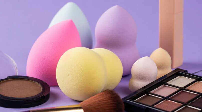 Beautyblenders en andere make-up producten op een paarse achtergrond.