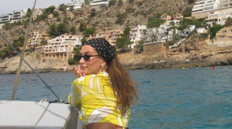 Hailey Bieber lacht naar de camera, terwijl ze op een boot vaart.