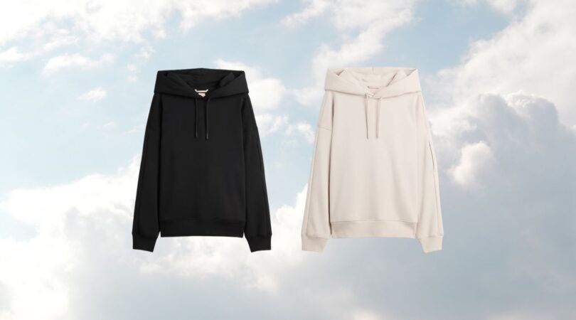 De Gap x BE&Iacute;S travel hoodie in zwart en beige, op een wolken achtergrond.